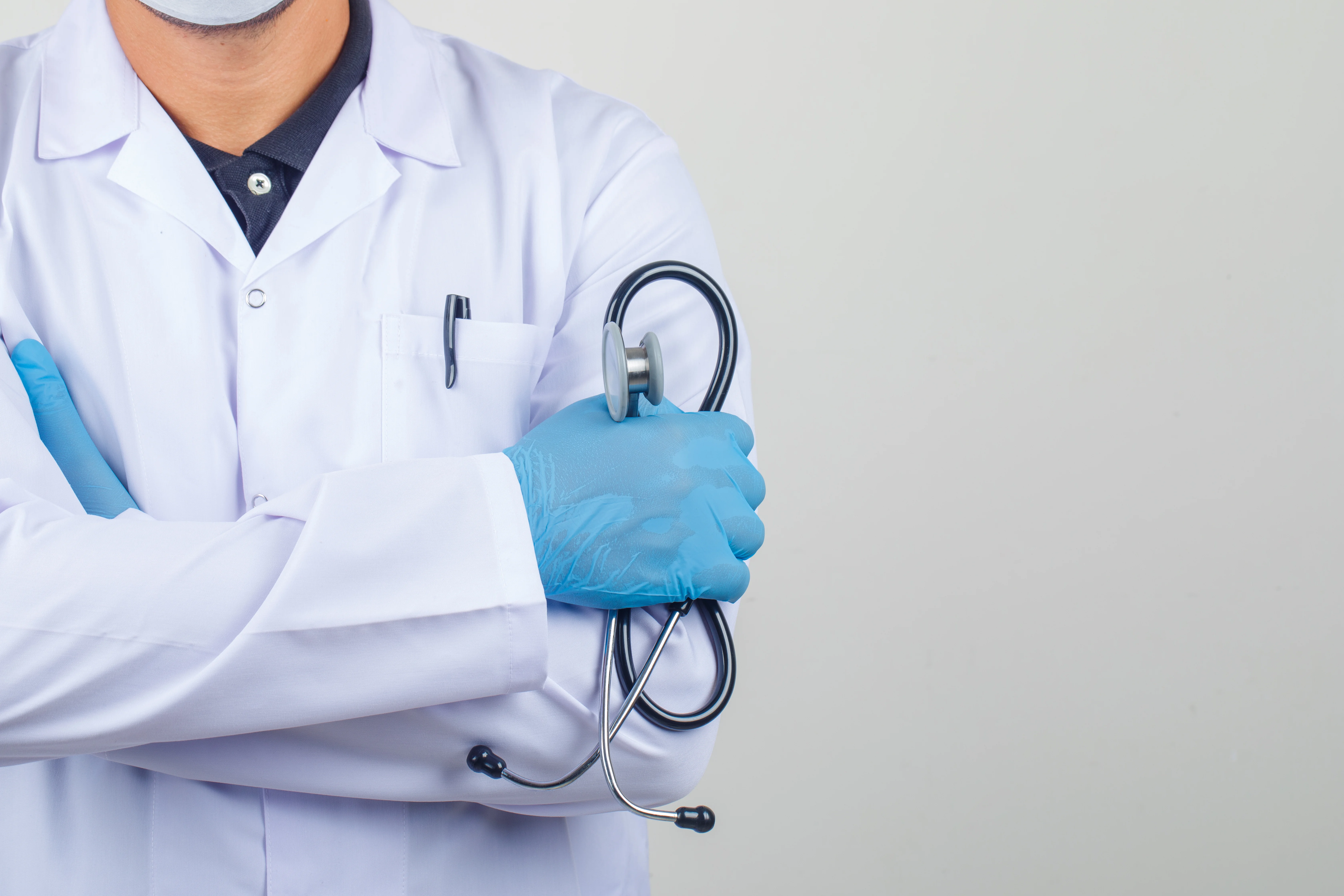 Tenaga medis memakai jas dokter putih dengan sarung tangan dan stetoskop di tangan